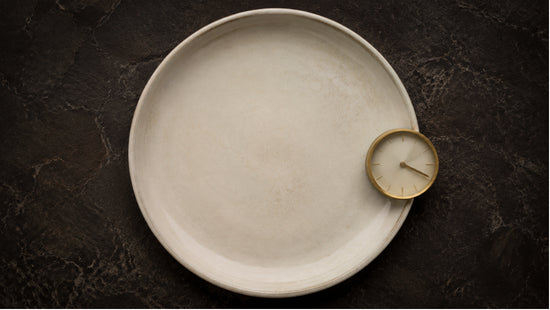 Top-down abstract photograph of an empty plate with a clock, representing the importance of timing when taking berberine before or after meals.
