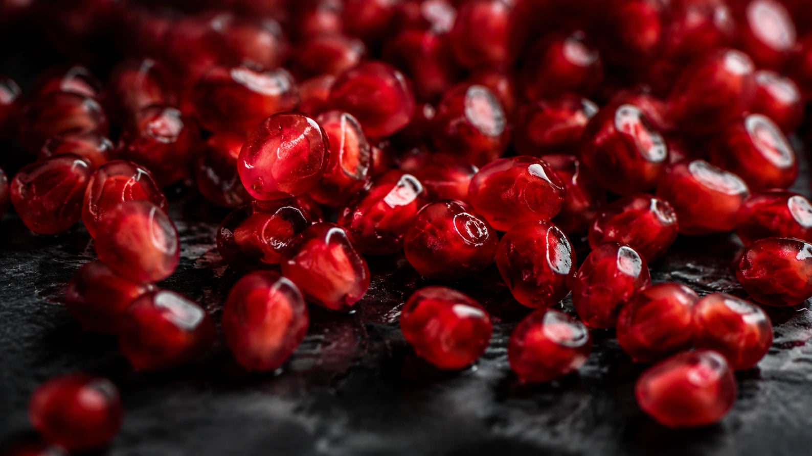 Close-up abstract photograph of glossy pomegranate seeds with dramatic lighting, symbolizing the hormonal and metabolic connection in PCOS.